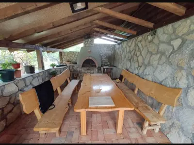 a wooden table and benches in a room with a stone wall at Village House Gracac in Ðurovići
