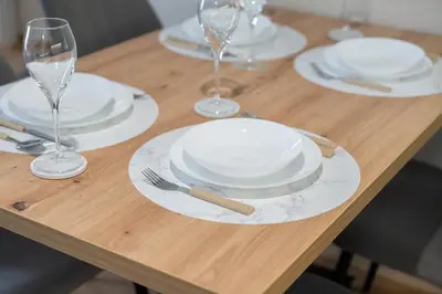 a wooden table with white plates and wine glasses at Duma Apartmani 2 Vrnjačka Banja in Vrnjačka Banja