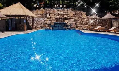 a large blue swimming pool with a stone wall at Grabak B3 in Vrnjačka Banja