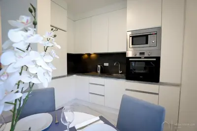a kitchen with white cabinets and a table with white flowers at Aqua Vista Lux Raj in Vrnjačka Banja