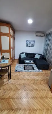 a living room with a black couch and a wooden floor at Apricus Mini Apartman Vrnjacka banja in Vrnjačka Banja
