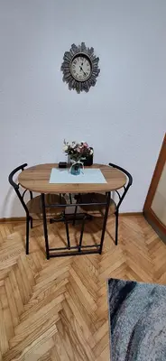 a table with a clock on the wall and a table with flowers at Apricus Mini Apartman Vrnjacka banja in Vrnjačka Banja