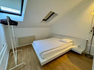 a small white bedroom with a bed and a window at Riseup apartman in Niš