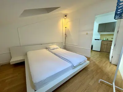 a white bed in a room with a kitchen at Riseup apartman in Niš