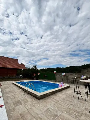 a swimming pool under a cloudy sky with a table at Vikendice Jovicic in Bukorovac