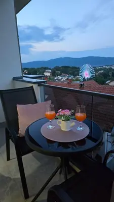 a table with two wine glasses and flowers on a balcony at Apartman NIKOLINA in Vrnjačka Banja