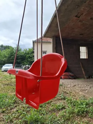 a red swing in front of a house at Tomić