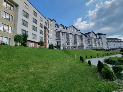 a large building with a grassy hill next to a river at Kopaonik, Milmari resort, Apartman Duga in Kopaonik