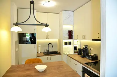a kitchen with white cabinets and a wooden table at Residence LUX in Niš