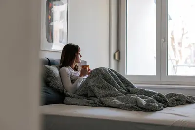 a woman laying in bed under a blanket holding a cup at WellNest Niš Self Check-in & Parking I Moderan, miran apartman plus radni kutak in Niš