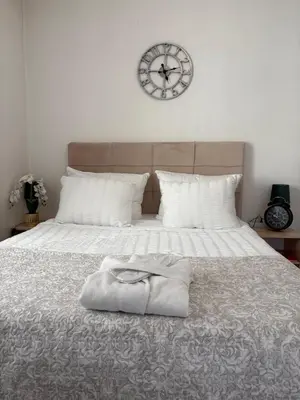 a bed with a white blanket and a clock on the wall at Wing Apartman Jagodina in Jagodina