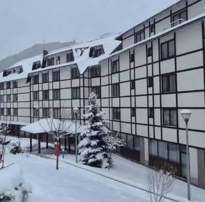 a snow covered building with a christmas tree in front of it at Apartman Nik Brzeće Kopaonik in Brzeće