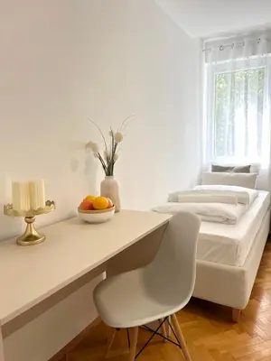 a white bedroom with a bed and a desk with a bowl of fruit at Talia in Niš