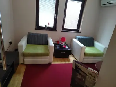 a living room with two white chairs and a red rug at Queen delux in Niš