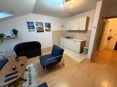 a living room with chairs and a table and a kitchen at ROOF Apartman in Jagodina