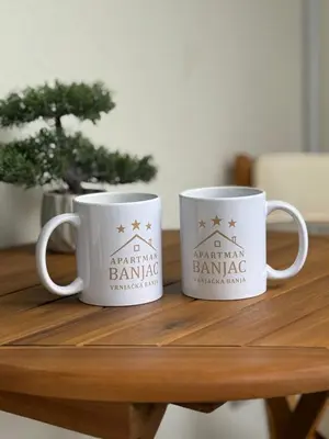two white coffee mugs sitting on a wooden table at Apartman Banjac in Vrnjačka Banja