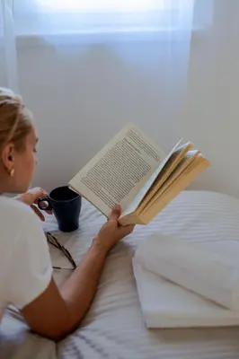 a woman sitting on a bed reading a book at LALA & DAUGHTERS Apartment in Vrnjačka Banja