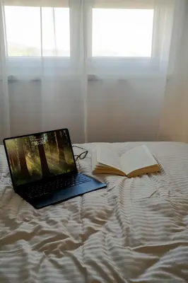 a laptop computer sitting on a bed with an open book at LALA & DAUGHTERS Apartment in Vrnjačka Banja