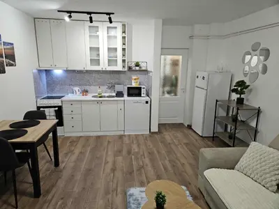 a kitchen with white cabinets and a living room at BK Apartment in Niš