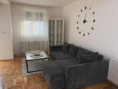 a living room with a couch and a clock on the wall at City Comfort Apartment in Vranje