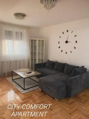 a living room with a couch and a clock on the wall at City Comfort Apartment in Vranje