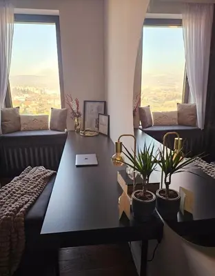 a living room with a table and two windows at Riviera Suite in Niš