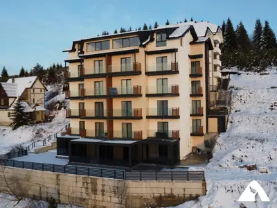 a building on a river in the snow at Apartman Oliver in Kopaonik