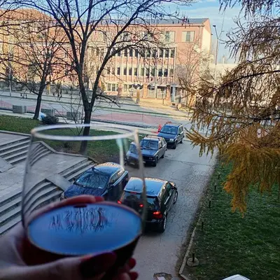 a hand holding a glass of wine with cars on a street at NoVa apartman - stan na dan in Vranje