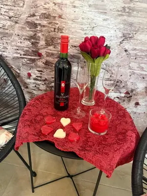 a red table with a bottle of wine and a vase of roses at Apartman Petra Sokobanja in Soko Banja