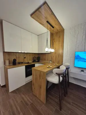 a kitchen with white cabinets and a table and a tv at Zira apartman in Vranje
