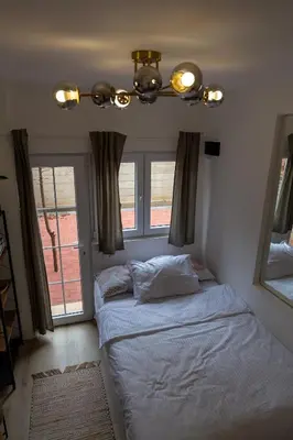 a bedroom with a bed with a chandelier and windows at Urban Nest Apartments in Niš