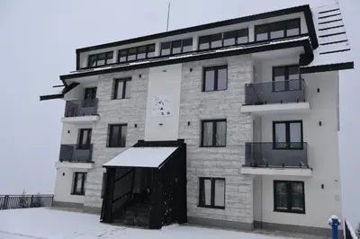 a white building with a black door in the snow at Apartmani Vidik,Treska in Kopaonik