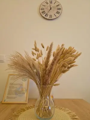 a vase with flowers in it on a table with a clock at Panoramic Nest in Vrnjačka Banja