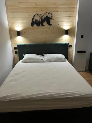 a bedroom with a large white bed with a wooden wall at SKI GOAT Kopaonik Centar vila Nikola in Kopaonik