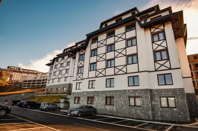 a tall white building with cars parked in a parking lot at Apartman B24 Vidik Residence in Kopaonik