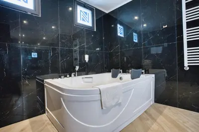 a white tub in a black tiled bathroom at Hotel Nais Nis Autoput in Niš