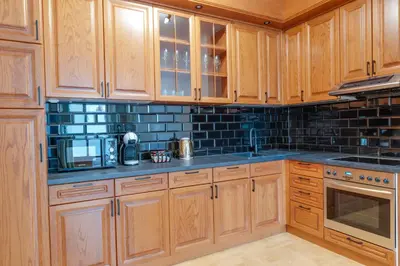a kitchen with wooden cabinets and black tiles on the wall at Apartmani Central 2 & Free Parking in Vrnjačka Banja
