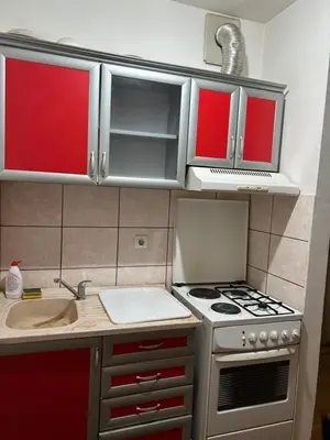 a small kitchen with a stove and red cabinets at Stan in Niš