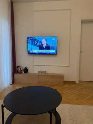 a living room with a table and a tv on the wall at Apartman Vrnjacka Banja in Vrnjci