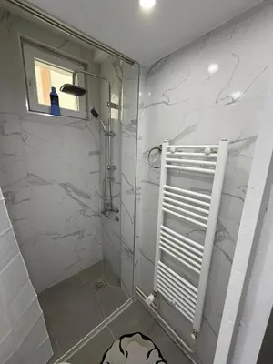 a bathroom with a shower with white marble walls at Apartman AURORA Trstenik in Trstenik