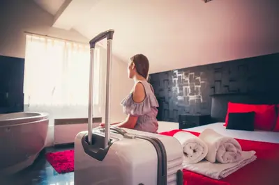 a woman is standing next to a bed with a suitcase at Guest House Vila Salute in Niš