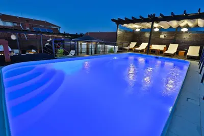 a blue swimming pool in a backyard at night at Garni Hotel Zen free parking in Niš