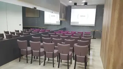 a conference room with pink chairs and a screen at Garni Hotel Niš City View & Spa in Niš
