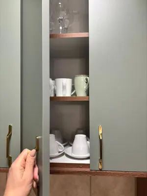 a person opening a cupboard door with plates and cups at Alex apartman in Vrnjačka Banja