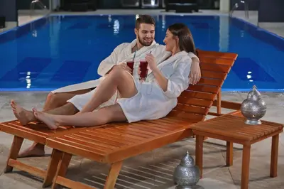 a man and woman sitting on a bench next to a pool at Zepter Spa Wellness Hotel & Zepterme member of Zepter Hotels in Vrnjačka Banja