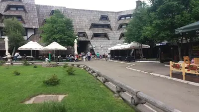 a building with umbrellas and people sitting in a park at Apartment Dunja Konaci in Kopaonik