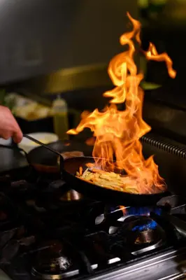 a person cooking food on a stove with flames at Hotel Tami Residence in Niš