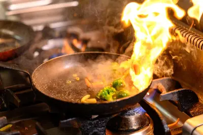 a wok with broccoli on a stove with flames at Hotel Tami Residence in Niš