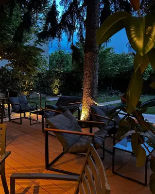 a deck with lounge chairs and a tree at night at Laguna Green Guest House in Niš
