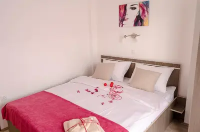 a bed with white sheets and red flowers on it at Apartmani Maja Sokobanja in Soko Banja